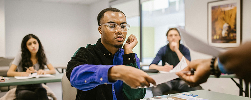 A black student handing in a multiple-choice paper, looking apprehensive