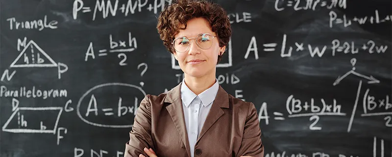 Expert teacher standing in front of a classroom chalkboard with mathematical equations.