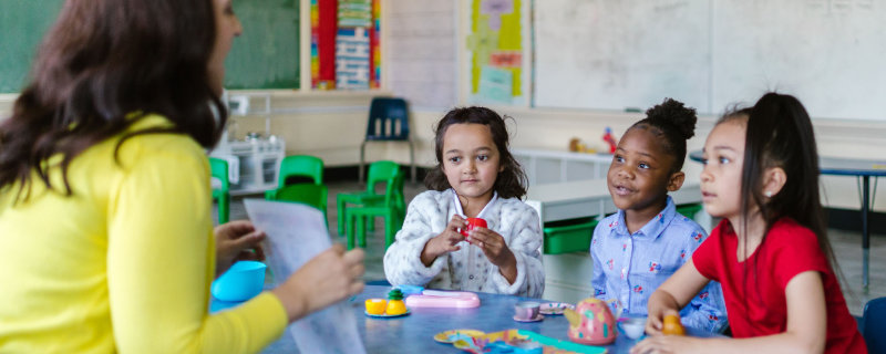 Three children learning to spell with Interleaving, watching their teacher who demonstrates on a piece of paper